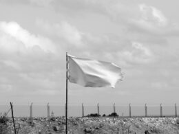 White flag waving in front of a fence (Unsplash, Pedro Farto)