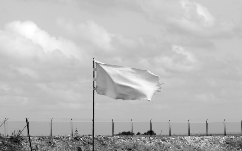 White flag waving in front of a fence (Unsplash, Pedro Farto)