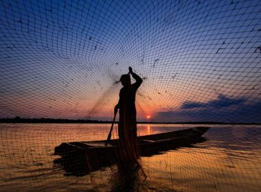 Man on a boat at dusk casting a fishing net